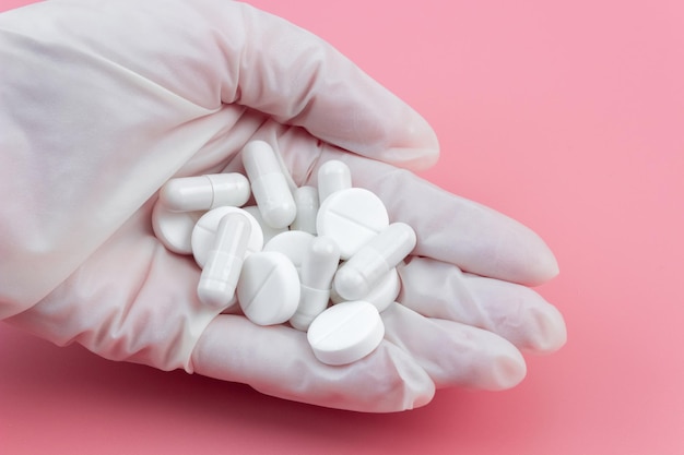 A pile of pills lies in a hand in a medical glove on a pink background. The concept of healthcare or medical care.