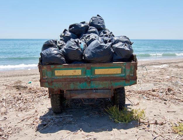 Pile of plastic bags in a tractor with ocean waves on a seashore