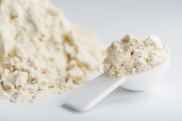 A pile of protein powder with a measuring spoon on a white background.