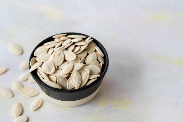 Pile of pumpkin seeds in bowl on white wooden background