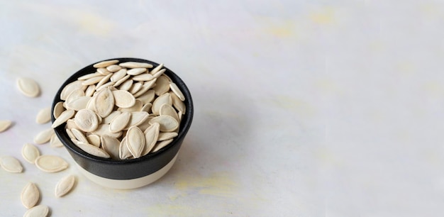 Pile of pumpkin seeds in bowl on white wooden background