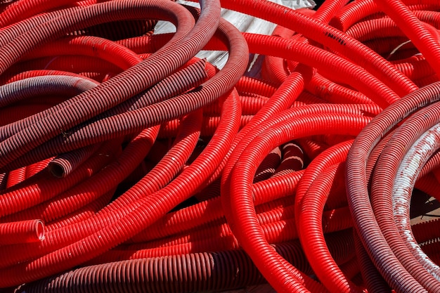 A pile of red corrugated PVC pipes for cable lay on the construction site full frame background