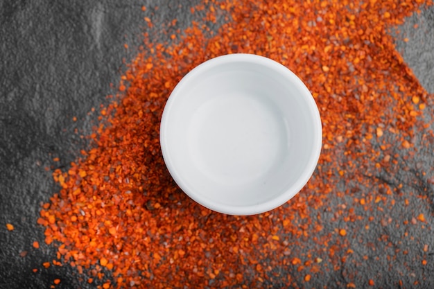 Pile of red ground cayenne pepper and white bowl on black. 