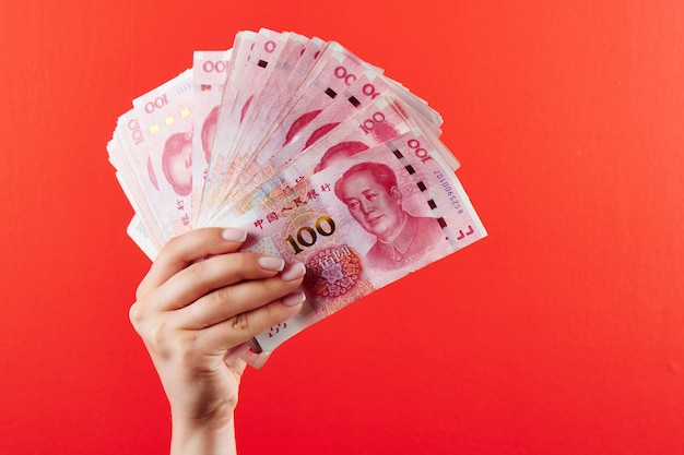 A pile of RMB banknotes of Chinese yuan money in a female hand on a red