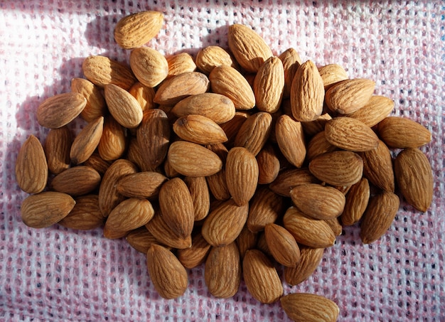 A pile of scattered almonds on a pink surface.