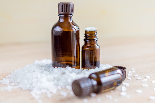 Pile of sea salt and bottles with aromatic essential oil on wooden table