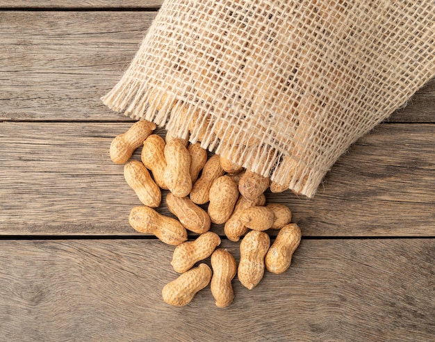 A pile of shelled peanuts in a bag over wooden table