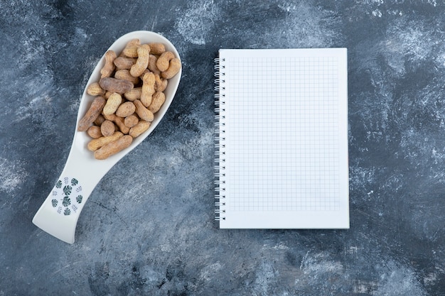 Pile of shelled peanuts with empty notebook over marble.