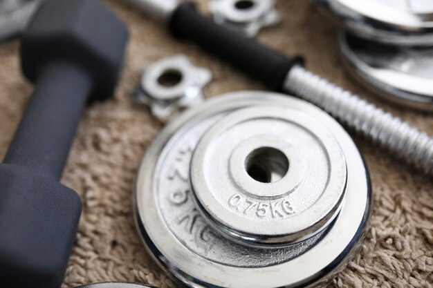 Pile of shiny chrome dumbbells disks lying around grip at home rug as domestic sport exercises