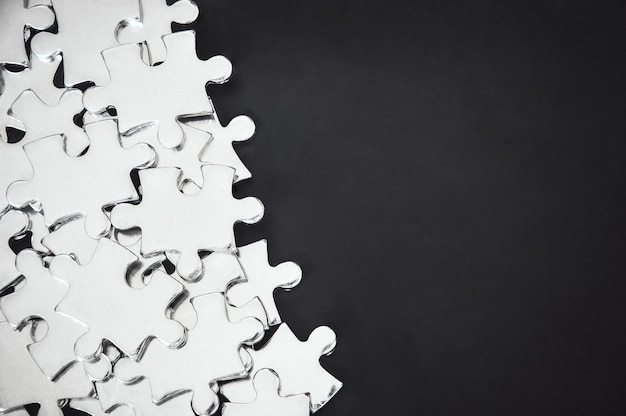 Pile of silver metal puzzle pieces on black color background