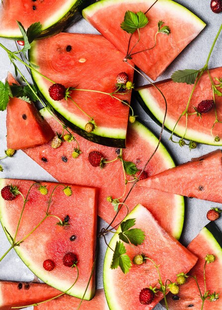 pile of sliced fresh watermelons and wild strawberries with green leaves