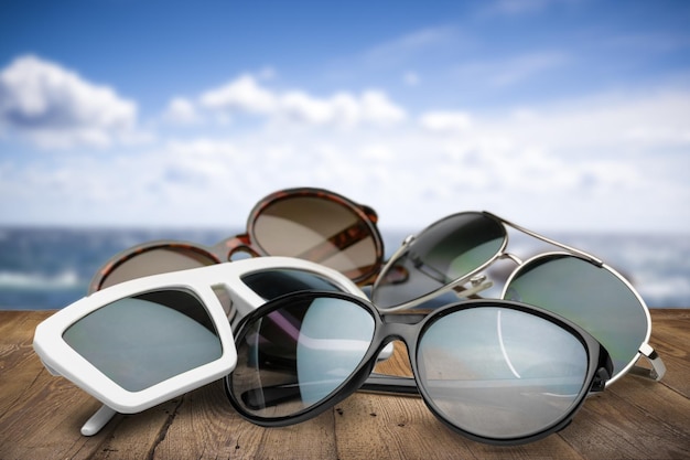 Pile of stylish sunglasses on beach background