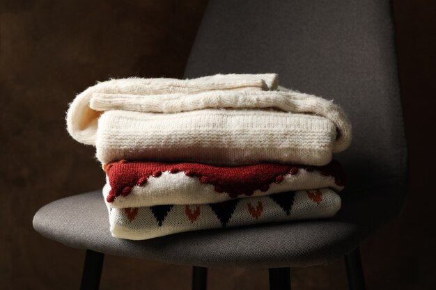 Pile of sweaters on chair against brown background