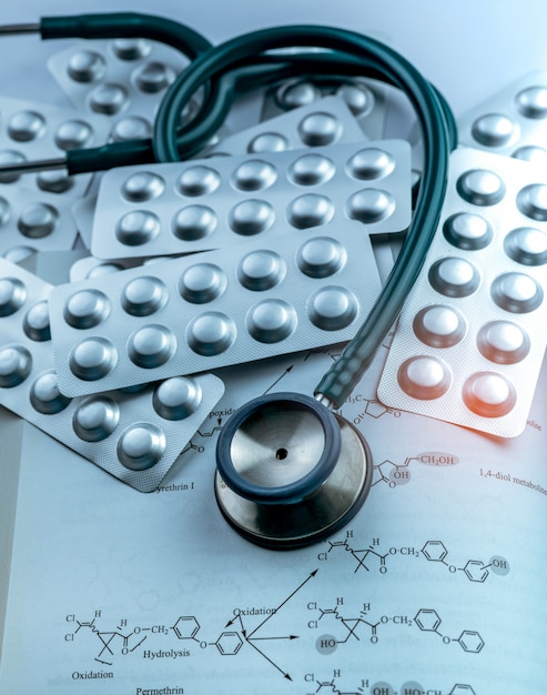 Pile of tablets pills in silver aluminium foil blister pack and stethoscope on textbook.  Pharmaceutical industry. Drug use in hospital. Healthcare.