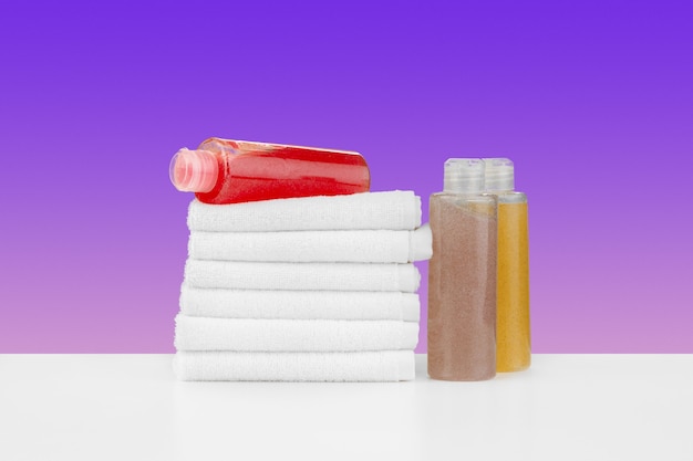 Pile of towels bottles with shampoo on white table