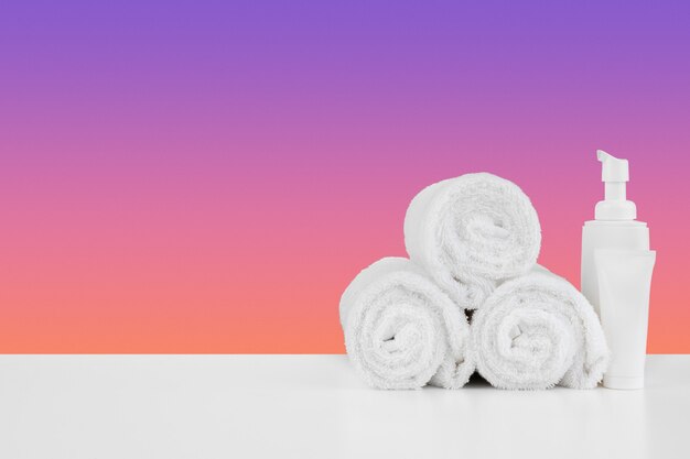 Pile of towels bottles with shampoo on white table