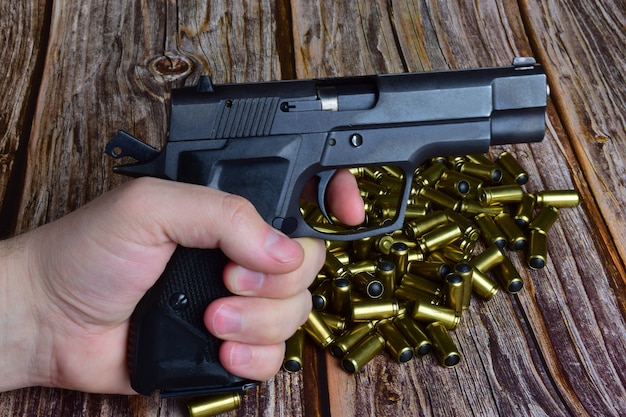 A pile of traumatic cartridges was piled on a brown wooden
background. against their background, a hand holds a pistol