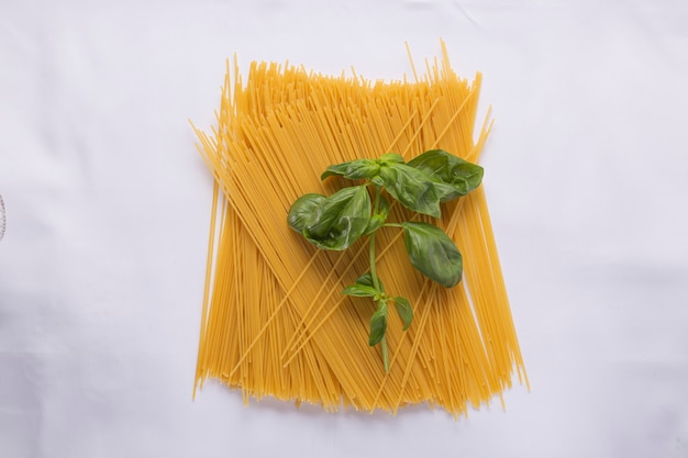 Куча сырых спагетти и листьев базилика на белой скатерти