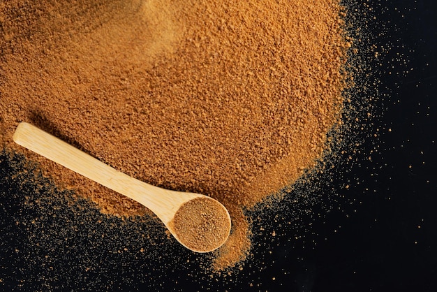 Pile unrefined cane brown sugar Panela with a wooden spoon on a black