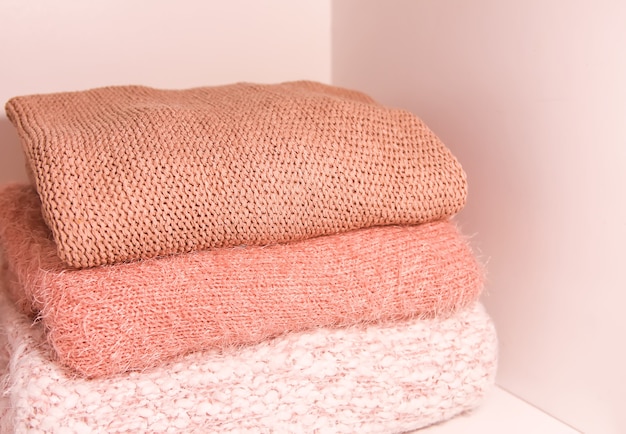 Pile of warm autumn and winter knitted sweaters on a home wardrobe shelf. Modern fashion clothes in shades of living coral.