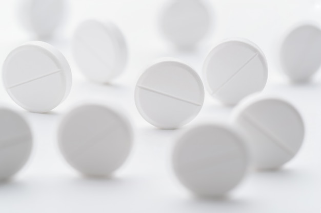 A pile of white pills scattered on a bright white background. Selective focus. Mockup layout, template.