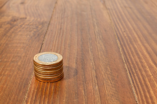 A pile with a lot of Real brazilian money coins stacked on a wood table