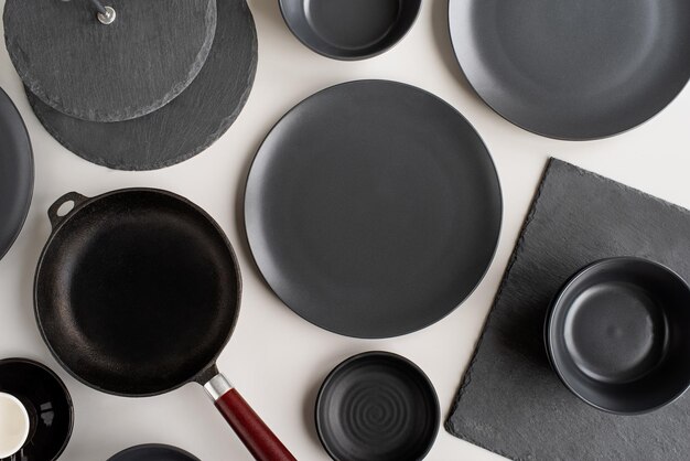 piles of black ceramic dishes and tableware top view on gray background