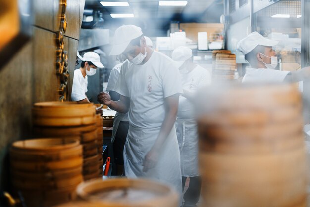 Piles of stacking bamboo steamers are steaming for dim sum in front of the restaurant with blur chefs in background.