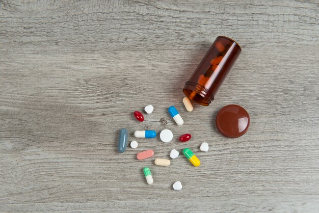 Pill background on a wood table that spilling out of pill bottle.