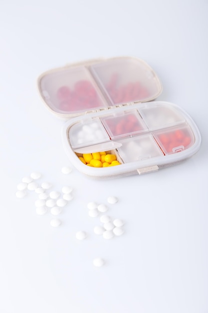 Pill box with colorful pills and vitamins Plastic beige container with cells for medicines Health concept Selective focus closeup