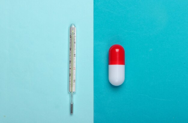 Pill capsule and thermometer on a blue background. Top view. Minimalism