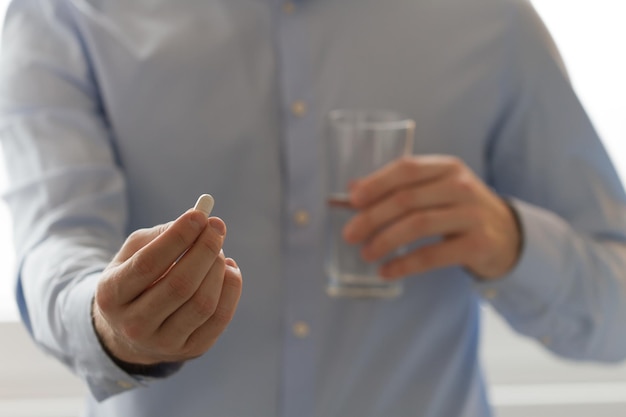 男性の手で錠剤と水の入ったグラス