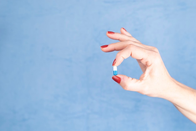 pill held by the fingers of a hand against blue background medical supplies