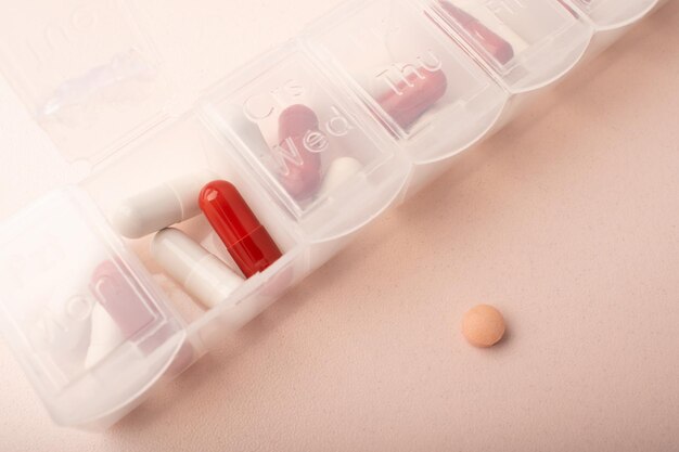 pillbox with pills and supplements on pink background top view capsules in daily organizer weekly pill organizer and pink pill clear plastic pill container and medications high quality photo