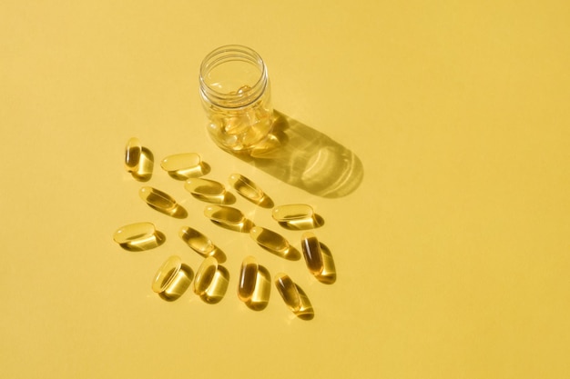 Foto pillen en glazen pilfles op gele achtergrond grote gouden tabletten omega 3 capsules dichtbij