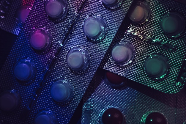 Pillen of geneesmiddelen in een verpakking onder neonlicht op een donker achtergrondpatroon voor ontwerp