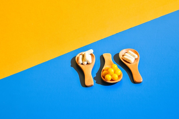 Pillen op houten lepel op blauwe en gele achtergrond. hard licht en schaduwen. modern isometrisch creatief minimalisme concept. vitaminen en prebiotica, probiotica. herfst vitamine dosis.