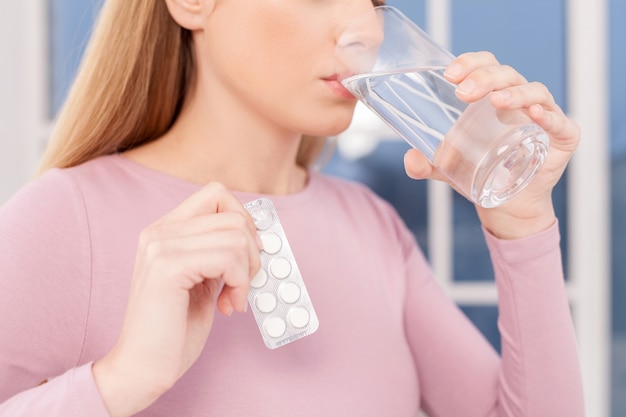 Pillen slikken. Bijgesneden afbeelding van jonge vrouw die pillen neemt en water drinkt