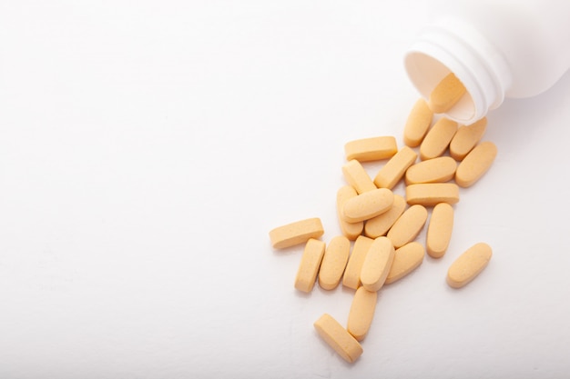 Pillen verspreid van vitamines van de flessen de oranje, ovale geneeskunde op witte achtergrond