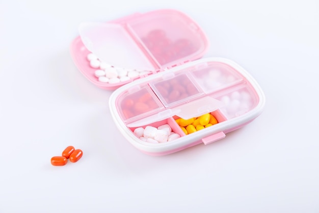 Pillendoosje met kleurrijke pillen en vitamines Plastic roze container met cellen voor medicijnen Gezondheidsconcept Selectieve focus close-up