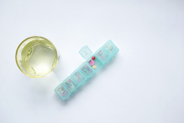 Pillendoosje vullen met medische capsule en glas op wit oppervlak