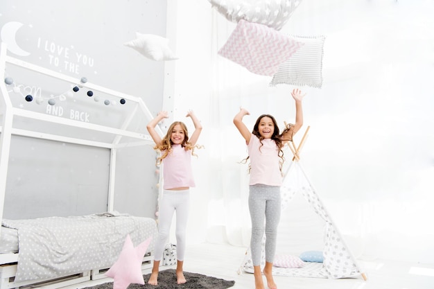 Pillow fight pajama party Evening time for fun Sleepover party ideas Girls happy best friends or siblings in cute stylish pajamas with pillows sleepover party Sisters play pillows bedroom party