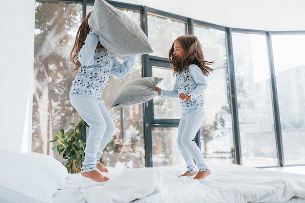 Pillow fight two cute little girls indoors at home together
children having fun