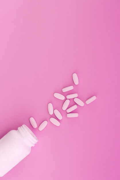 Pills are poured from a white bottle on a pastel pink background. Place for text.Flat lay.