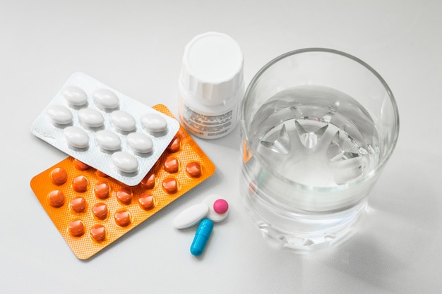 ブリスター、カプセル、白い背景の上の水のガラスの丸薬。風邪、ビタミン、健康複合体の治療のための準備