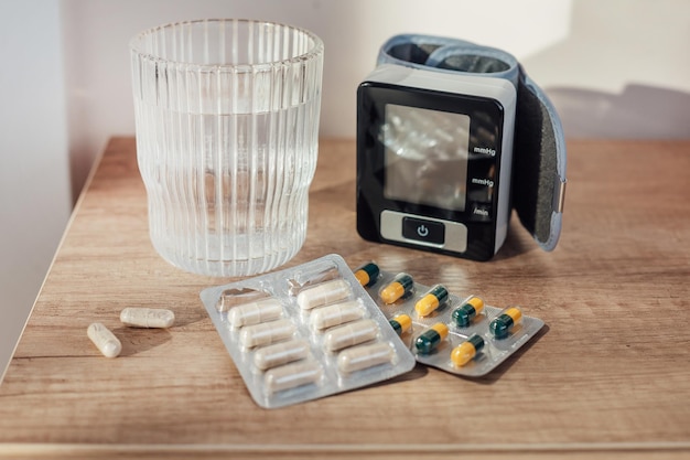 Pills capsules glass of water and digital blood pressure monitor on wooden background