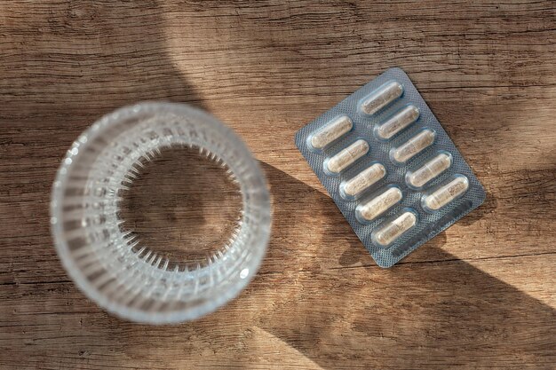 Foto pillole capsule medicina e bicchiere d'acqua su fondo di legno