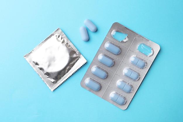 Pills and condom on light blue background flat lay Potency problem