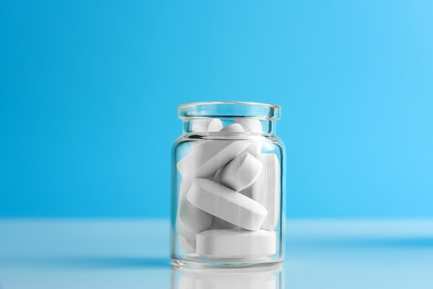 Pills in a glass bottle on a blue background with copy space