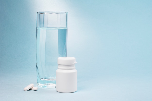 Pills and glass of water on blue background